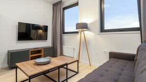 A modern living room with a flat-screen TV, a wooden coffee table, a floor lamp, and a grey sofa. - EIR One Bedroom Apartments (Reykjavík)