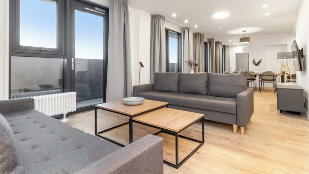 Ein modernes Wohnzimmer mit grauem Sofa, einem Holztisch und einem Essbereich mit Tisch und Stühlen.