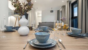 Ein Essbereich mit einem Holztisch, gedeckt für vier Personen, mit blauen Keramiktellern und -schüsseln, einer weißen Vase mit Trockenblumen und einer modernen Pendelleuchte.