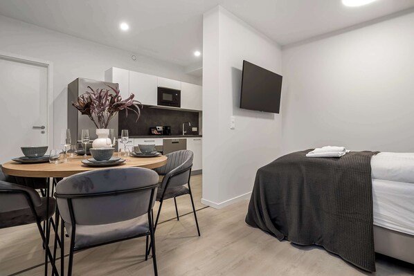 Quarto de hotel moderno com área de jantar, cozinha compacta e cama com cobertor.