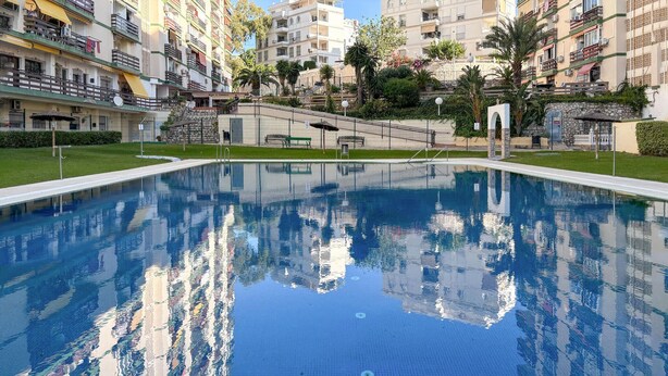 A swimming pool surrounded by multi-story buildings with balconies, a small garden area, and a stone staircase leading to an upper level. - Awesome apartment in Benalmadena (Benalmadena)