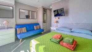 A hotel room with a bed, a blue sofa, a desk with a lamp, a TV on the wall, and a mirror. - Awesome apartment in Benalmadena (Benalmadena)