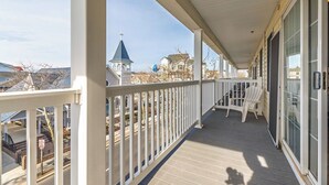 A covered balcony with white railings, a white chair, and a view of a church steeple and houses in the background. - Cute, spacious 4-bedroom townhouse with free WiFi and easy access to shops located downtown on the ocean block! (Ocean City)