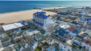 An aerial view of a coastal town with a prominent hotel featuring a blue roof, situated near a beach and a pier. - Cute, spacious 4-bedroom townhouse with free WiFi and easy access to shops located downtown on the ocean block! (Ocean City)