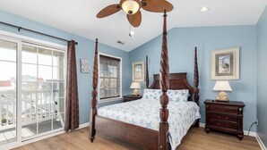 A four-poster bed with a ceiling fan, a nightstand with a lamp, and a window with blinds. - Cute, spacious 4-bedroom townhouse with free WiFi and easy access to shops located downtown on the ocean block! (Ocean City)