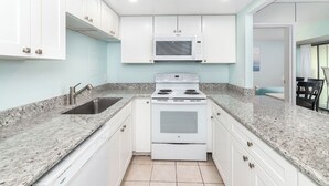 Une cuisine avec des meubles blancs, un plan de travail en granit, un four à micro-ondes encastré et une cuisinière.