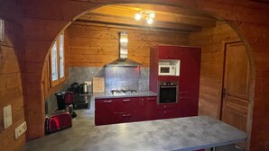 A kitchen with wooden walls, a central island, a stove, a microwave, and a red cabinet.