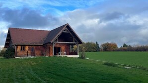 A wooden house with a sloped roof, a porch, and a large green field in the foreground.