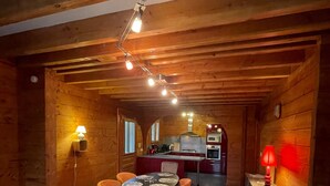 A wooden interior with a dining area, kitchen, and a red lamp.