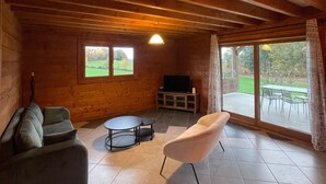 A cozy room with a wooden ceiling, a sofa, a chair, a small table, and a TV.