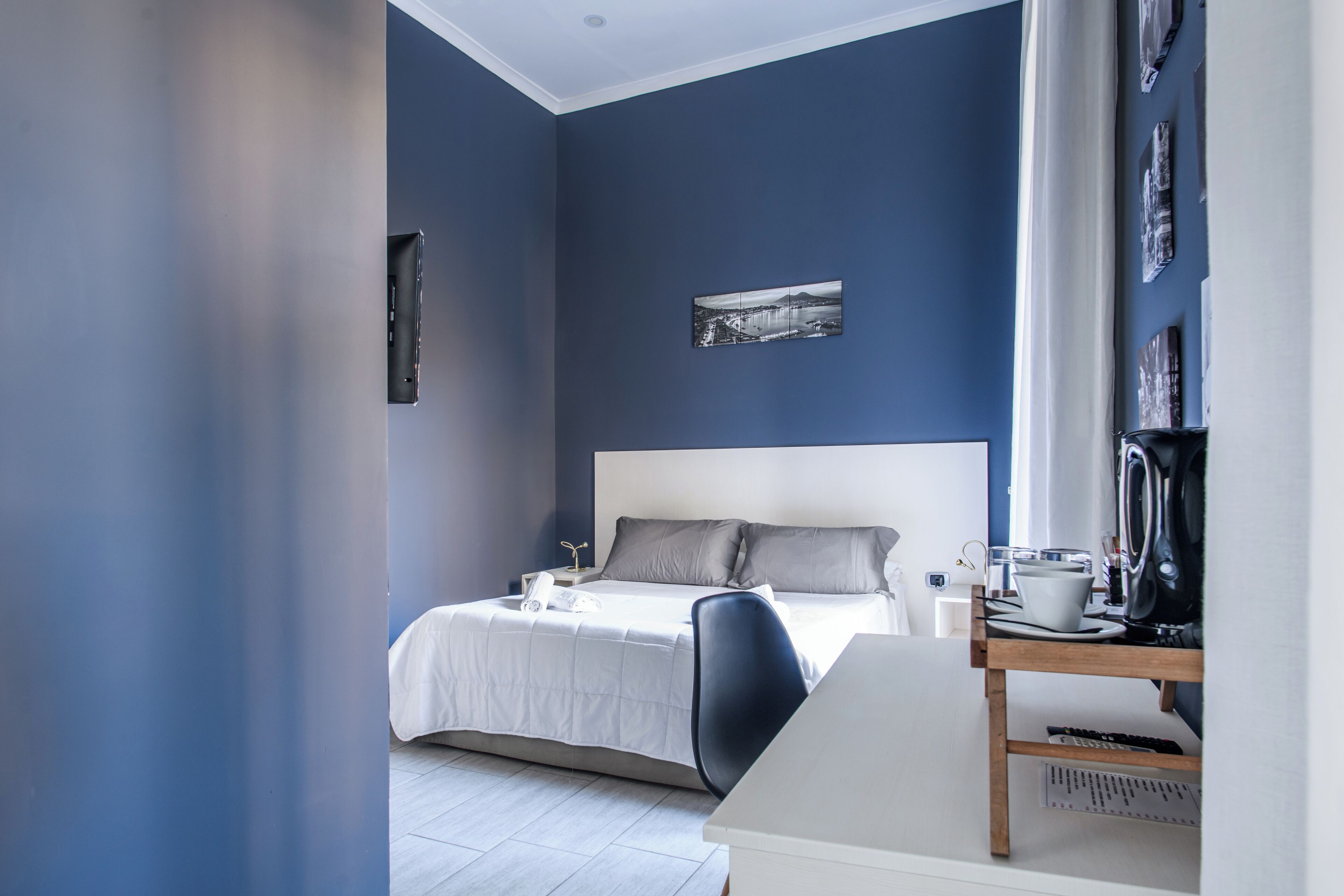 A modern bedroom with a large bed, a desk, and a coffee maker.
