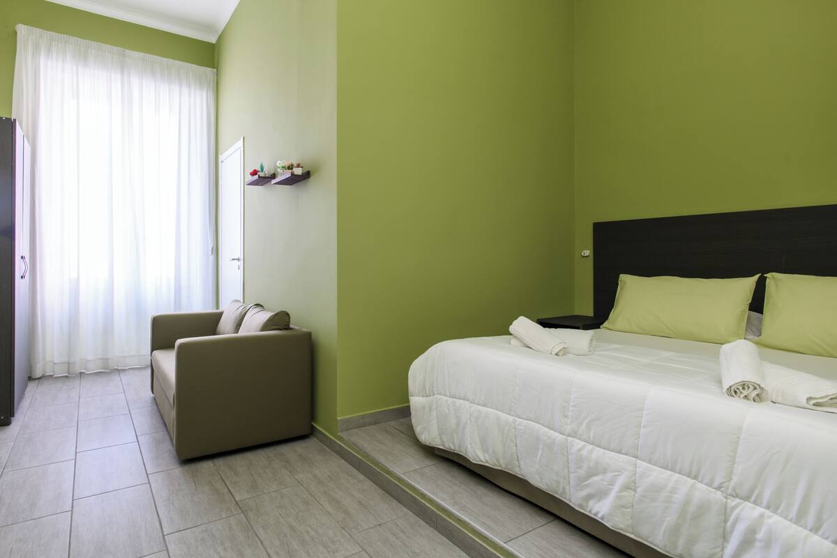 A hotel room with a bed, a sofa, and a window with curtains.