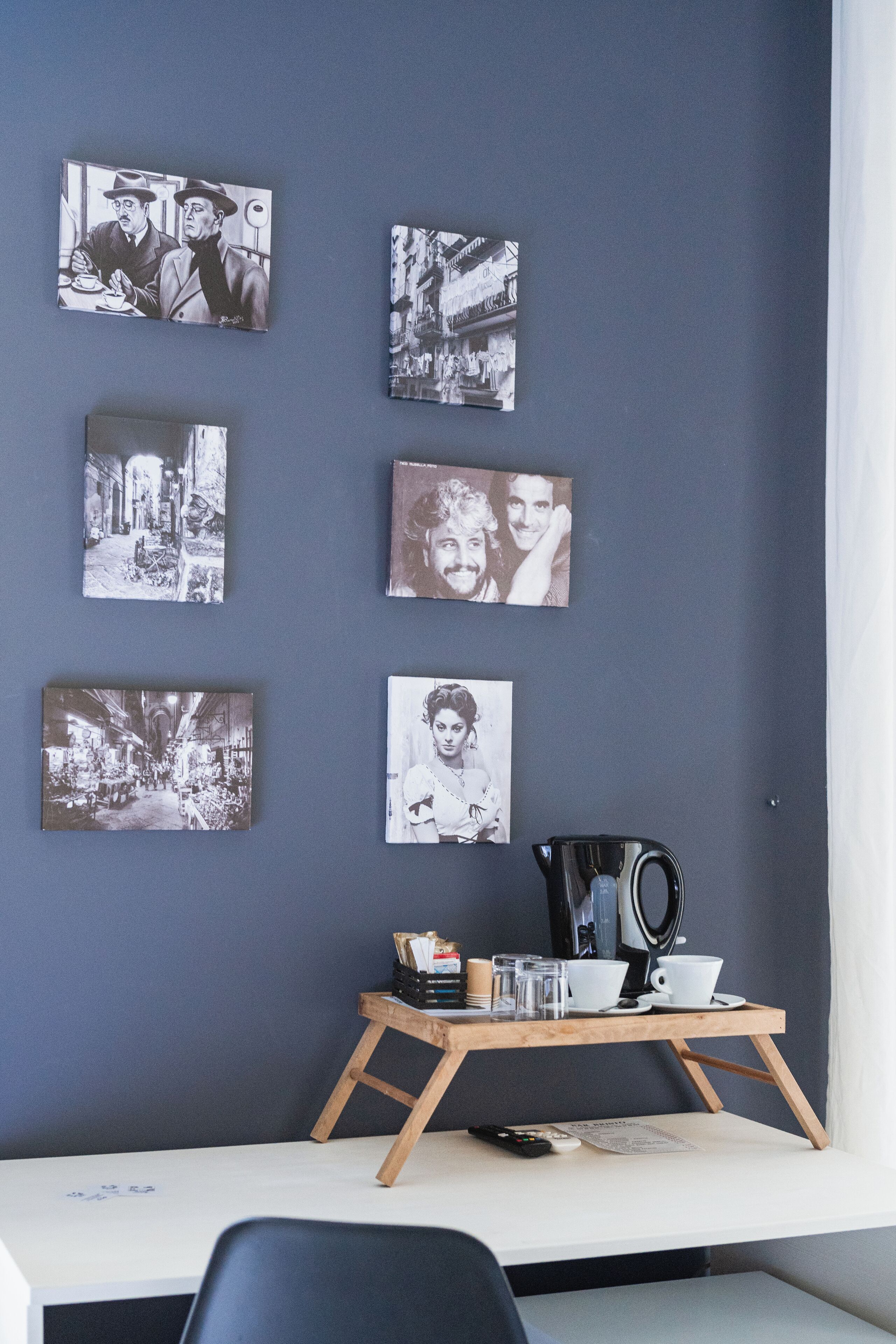 A room with a dark blue wall, a wooden coffee table with cups and a coffee pot, and six black-and-white photographs on the wall.