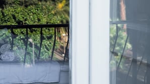 A view from a window with a balcony, featuring a neatly made bed and a lush green tree outside. - Holiday Naples art room   (Naples)