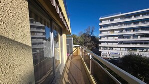 Een balkon met uitzicht op een meerlaags gebouw, een helderblauwe lucht, en een gedeeltelijk zicht op een gebouw met een 'P'-bord.
