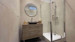 Un baño moderno con un espejo redondo, un lavabo sobre encimera, un mueble de tocador de madera y una ducha con mampara de cristal.