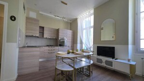 Una cocina moderna con electrodomésticos integrados, un comedor con mesa redonda y un televisor sobre un mueble blanco.