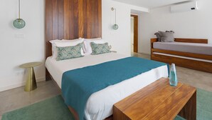 A modern bedroom with a wooden headboard, a bed with a teal bedspread, a bedside table with a vase, and a bench. - Room 'Quarto 1 - Quádruplo Com Vista Mar' with Sea View, Wi-Fi and Air Conditioning (Santa Bárbara)