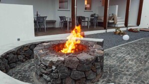 Un hogar de piedra con fuego encendido en el centro, rodeado por un muro de piedra.