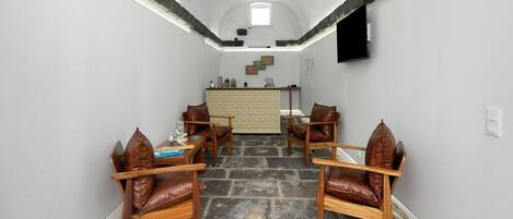 A room with a stone floor, wooden chairs, a small table, a white wall, and a window.