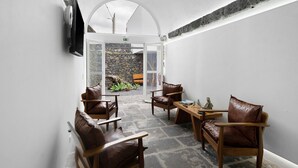 Una habitación con suelo de piedra, sillones de cuero, una mesa de madera y un televisor fijado a la pared.