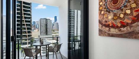 A balcony with a city view, a glass door, and a patterned artwork on the wall.