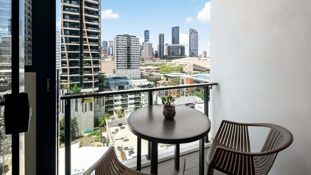 Ein Balkon mit Blick auf eine Stadtlandschaft, darunter moderne Gebäude und ein klarer Himmel.