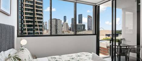 Una habitación de hotel con cama, ventana con vista a la ciudad, escritorio y silla.