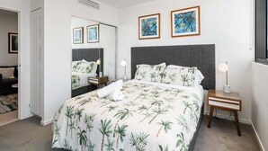 Ein modernes Schlafzimmer mit einem großen Bett, einem Nachttisch mit Lampe und zwei gerahmten Kunstwerken an der Wand.