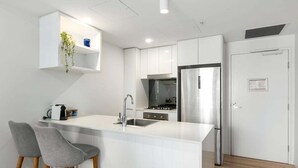 Eine moderne Küche mit weißen Schränken, einem Edelstahlkühlschrank, einem eingebauten Backofen und einer kleinen Bar mit zwei grauen Stühlen.