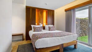 A bedroom with a large bed, wooden headboard, and a view of a stone wall and greenery outside. - Room 'Quarto 5 - Duplo Com Pátio' with Mountain View, Wi-Fi and Air Conditioning (Santa Bárbara)