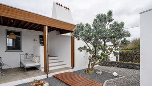 Une maison moderne dotée d’une terrasse en bois, d’un petit jardin avec un arbre et d’une façade blanche.
