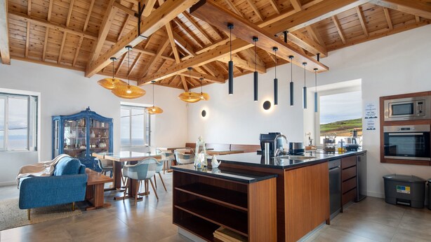 Une cuisine moderne avec des poutres en bois, des luminaires suspendus, un îlot central et des appareils électroménagers intégrés.