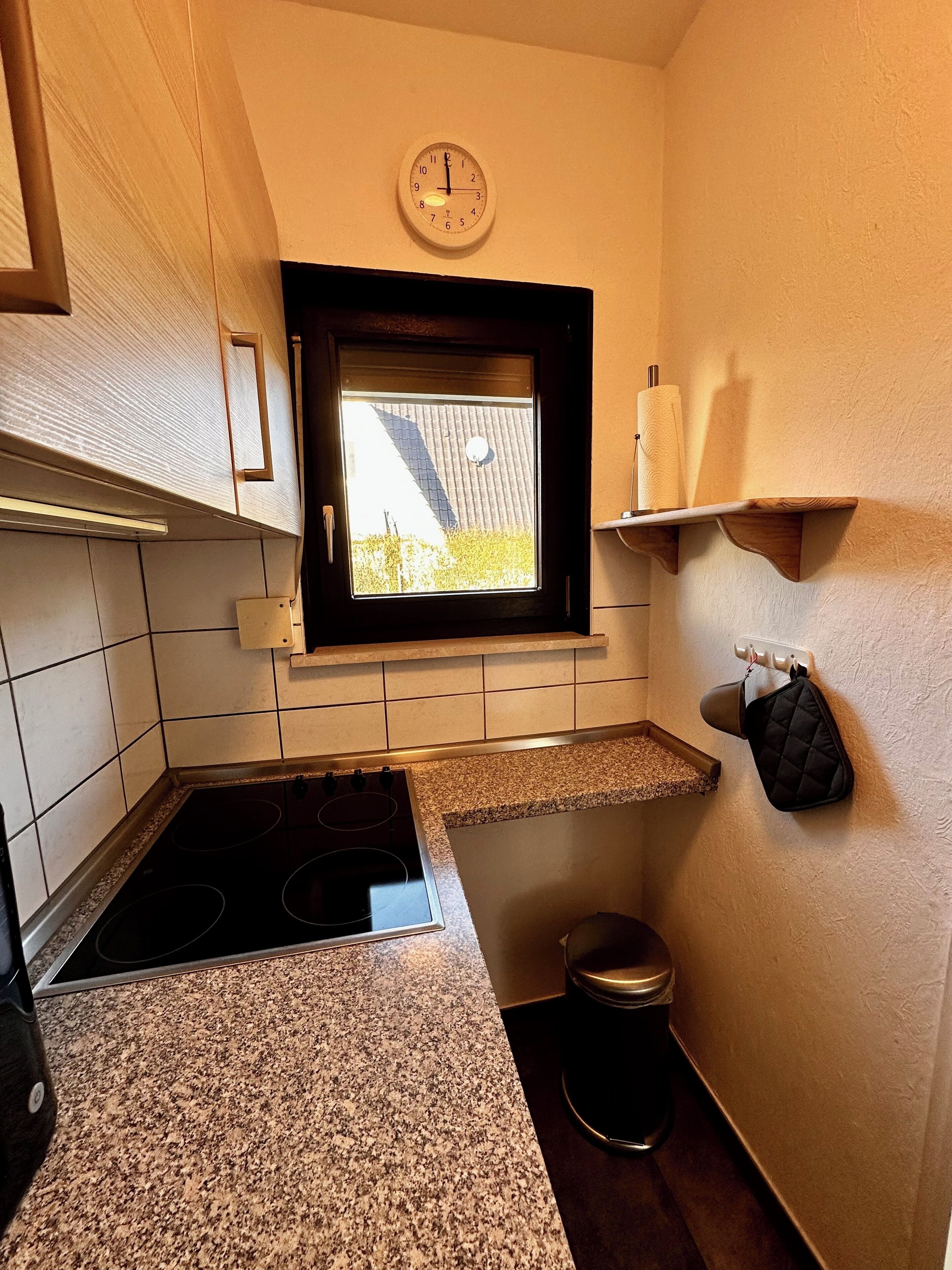 Una cocina compacta con ventana, estufa y un pequeño cubo de basura.