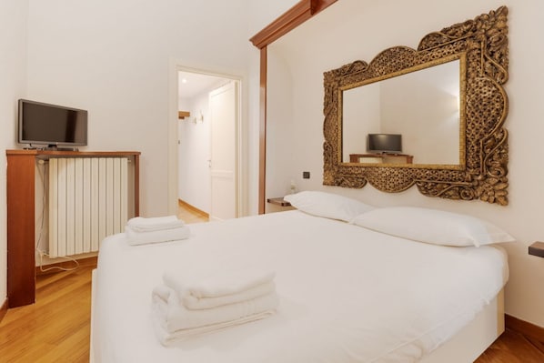 A hotel room with a bed, a television on a stand, a large ornate mirror, and a door leading to another room.