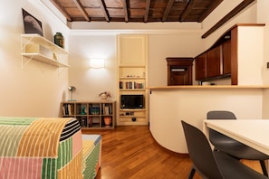 A compact kitchen with wooden cabinets, a dining table, and a bookshelf.