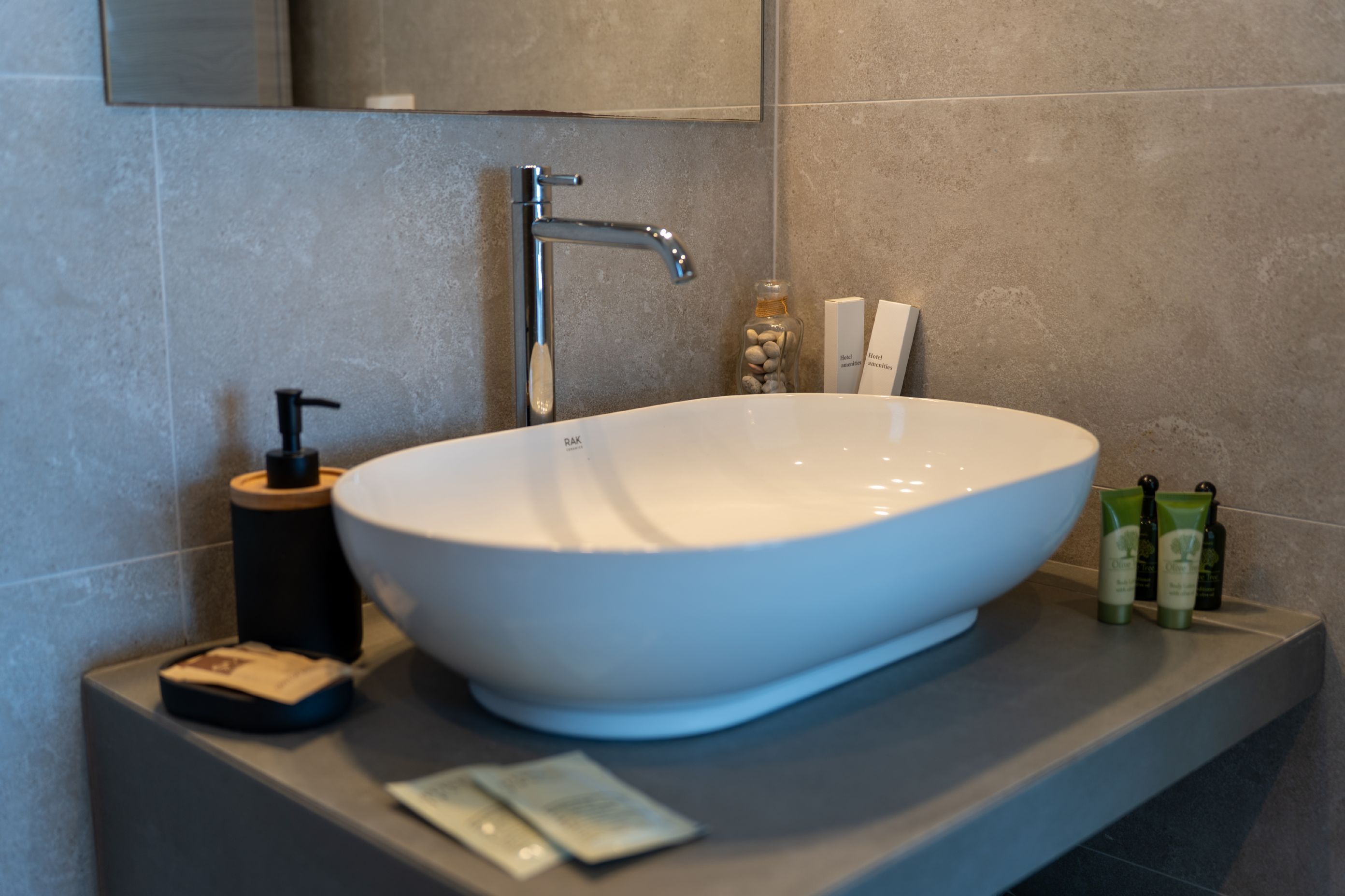 Un baño moderno con un lavamanos blanco de diseño, un cabezal de ducha manual y una pequeña botella de jabón sobre el mostrador.