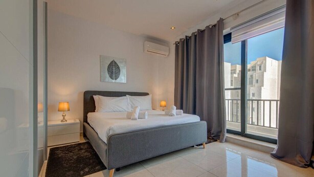 A modern hotel room with a large bed, two bedside lamps, a window with curtains, and a city view. - 3BR Penthouse w/ private Jacuzzi in St Julian’s (St. Julian`s)
