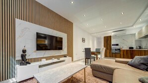 A modern living room with a flat-screen TV, a sofa, a coffee table, and a dining area with a chair. - 3BR Penthouse w/ private Jacuzzi in St Julian’s (St. Julian`s)