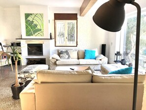 A living room with a sofa, a coffee table, a fireplace, a large window, and a plant.