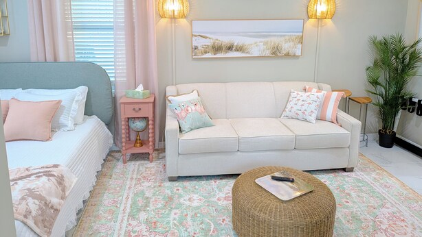 A bedroom with a bed, a sofa, a bedside table with a lamp, and a wall-mounted air conditioner. - Heavenly Hideaway Unit 1 (Daytona Beach)