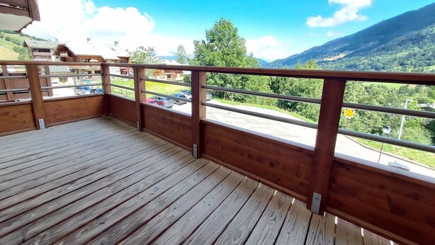 Une terrasse en bois avec une rambarde en métal, offrant une vue sur un paysage montagneux.