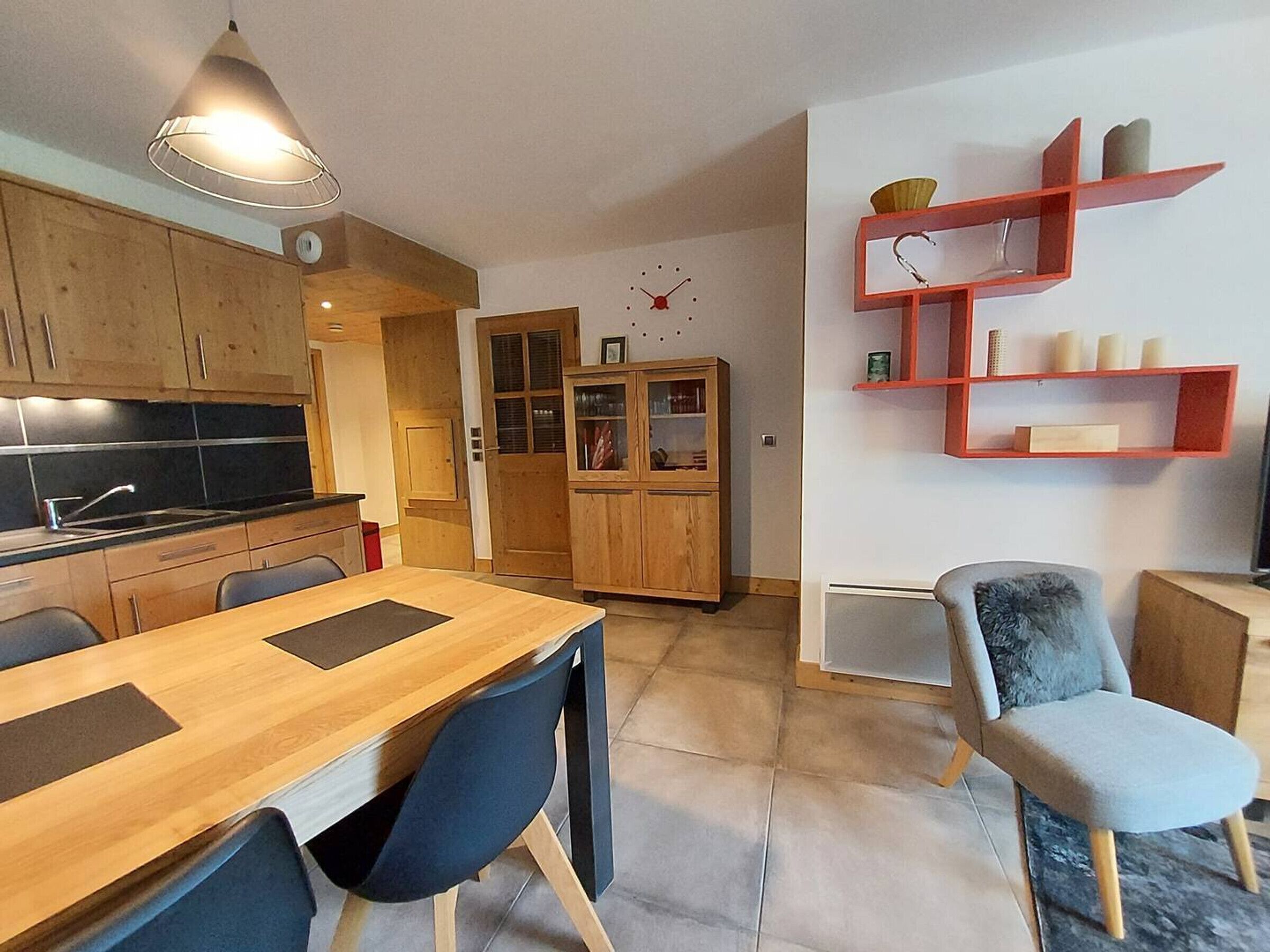 A modern kitchen with wooden cabinets, a dining table with chairs, and a red shelving unit against the wall.