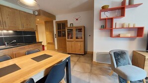 Une cuisine moderne avec des meubles en bois, une table à manger avec des chaises et une étagère rouge adossée au mur.