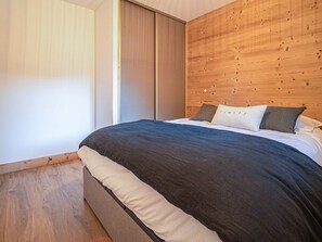A bedroom with a wooden headboard, a large bed with dark bedding, and a sliding door. - Cozy 4-person apartment in Valmorel with balcony and parking (Valmorel)