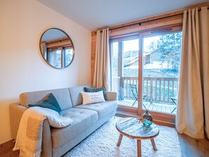 A cozy living room with a sofa, a round coffee table, and a large window with curtains. - Cozy 4-person apartment in Valmorel with balcony and parking (Valmorel)