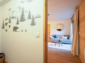 A room with a wooden floor, a light blue sofa, a round mirror, and a wall decal of a forest scene. - Cozy 4-person apartment in Valmorel with balcony and parking (Valmorel)