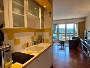 A compact kitchen with a built-in stove, a sink, and a dining area with a table and chairs. - Charming studio on the slopes in Villard-de-Lans (Villard-de-Lans)