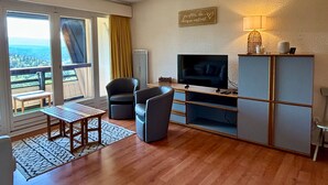 Un salon moderne doté d’un téléviseur, de sièges et offrant une vue sur l’extérieur.