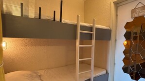 Un lit superposé avec une échelle, une porte avec une pancarte et un miroir hexagonal accroché au mur.